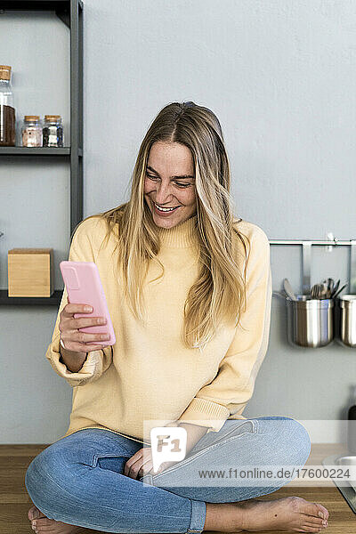 Smiling woman using smart phone in kitchen