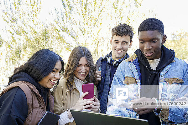 Cheerful students with smart phone and laptop on campus