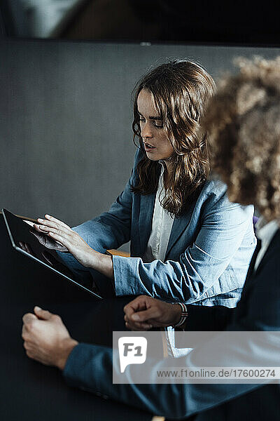 Geschäftsfrau sitzt neben einem Kollegen am Schreibtisch im Coworking-Büro und nutzt einen Tablet-PC