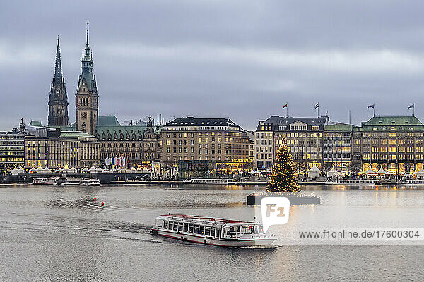 Germany  Hamburg  Tourboat sailing across Inner Alster Lake with Christmas tree and city buildings in background
