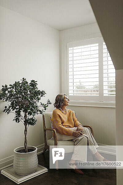 Frau sitzt auf einem Stuhl und schaut zu Hause durch das Fenster