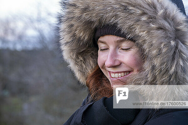 Young woman in fur hooded coat smiling with eyes closed