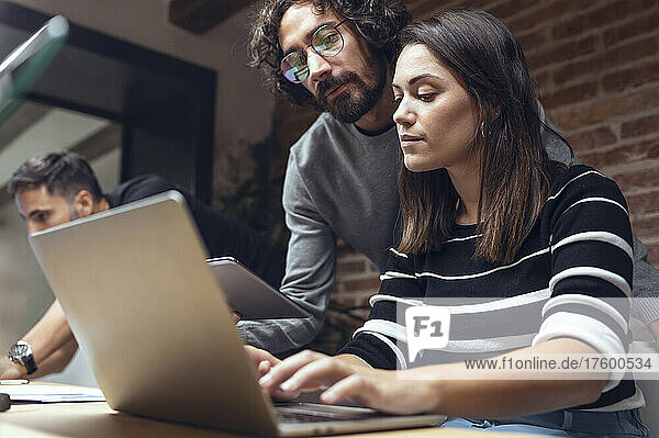 Businessman and businesswoman discussing on laptop in coworking office
