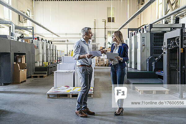 Businessman and businesswoman sharing ideas standing in factory
