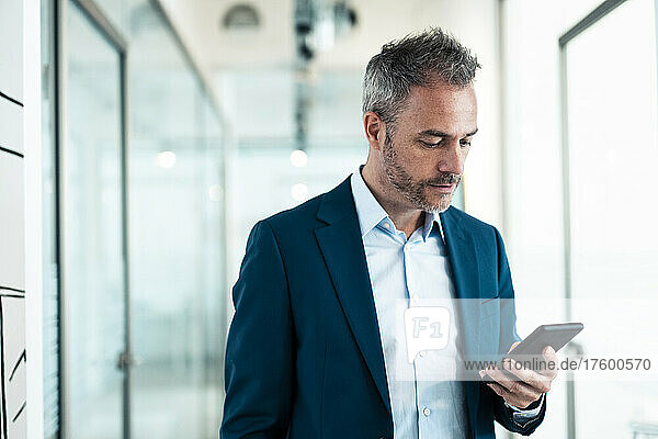 Businessman using smart phone in corridor at office