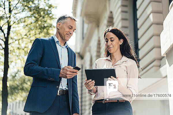 Businesswoman discussing with businessman over tablet PC on sunny day