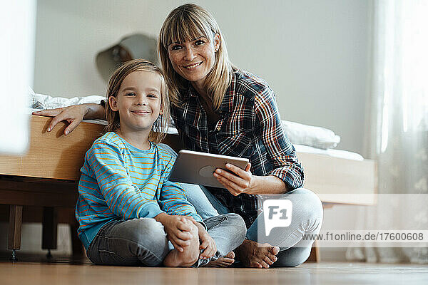 Lächelnde Frau und Sohn mit Tablet-PC im Schlafzimmer zu Hause