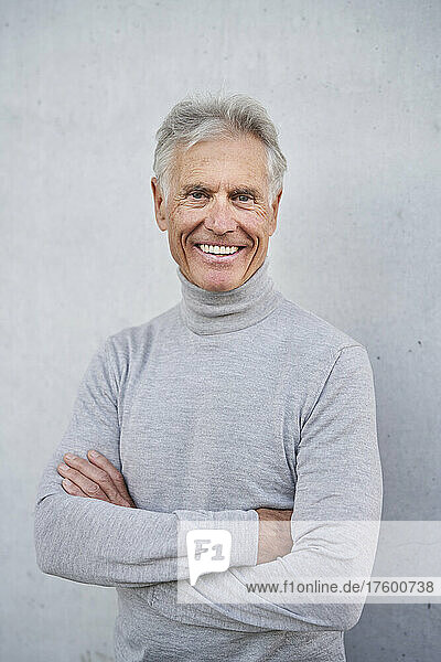 Happy senior man with arms crossed in front of wall