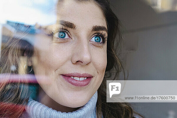 Thoughtful woman with blue eyes seen through glass