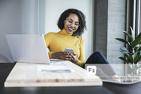 Smiling businesswoman text messaging on smart phone in office