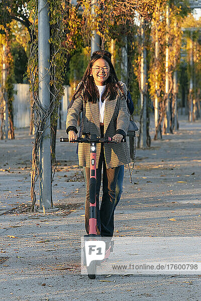 Smiling businesswoman riding electric push scooter with businessman behind her on road