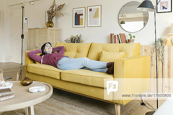 Glückliche Frau mit den Händen hinter dem Kopf entspannt auf dem Sofa im Wohnzimmer