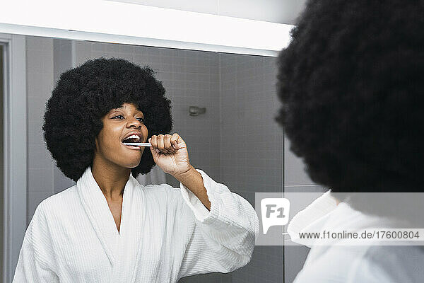 Afro woman brushing teeth and looking in mirror at home