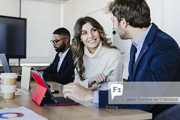 Lächelnde Geschäftsfrau diskutiert mit Kollegen im Coworking-Büro