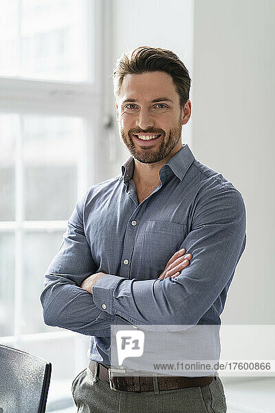 Happy businessman with arms crossed standing in office