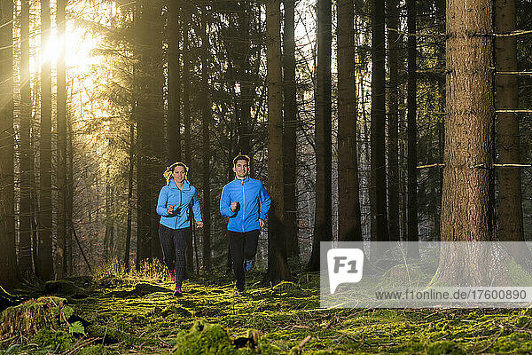 Man and woman jogging in forest at sunset