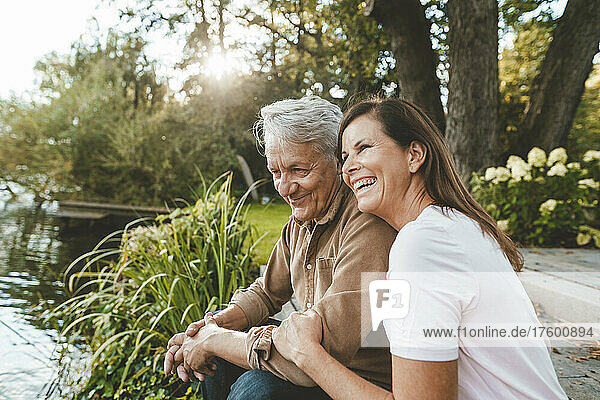 Fröhliche Frau sitzt mit älterem Mann am See