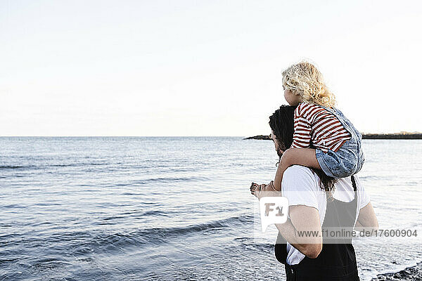Man carrying son on shoulders by seashore at beach