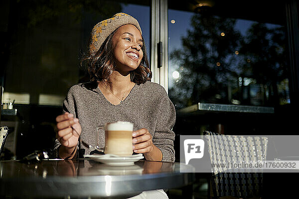 Young woman with coffee laughing at sidewalk cafe