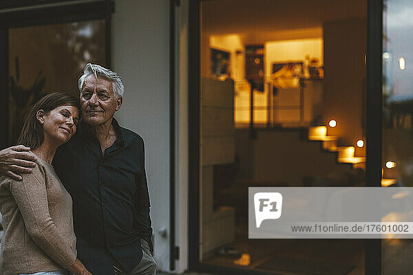 Senior man with woman standing in front of house at dusk