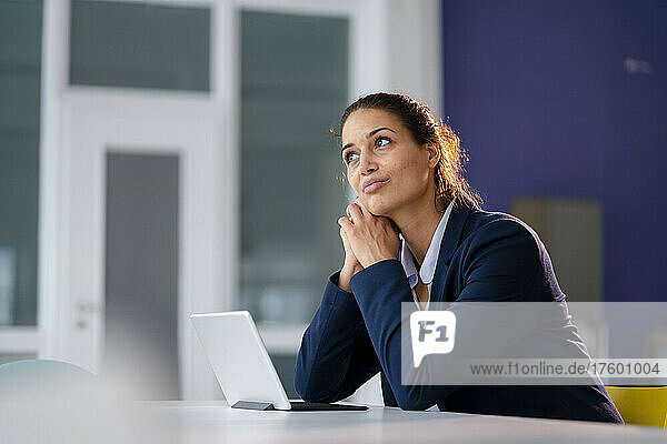 Businesswoman sitting with tablet PC day dreaming at desk