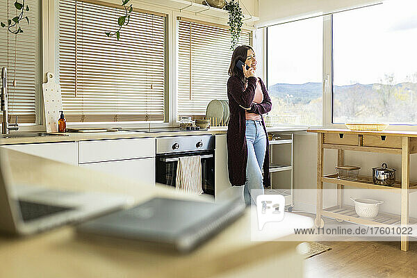 Frau telefoniert zu Hause in der Küche mit Smartphone