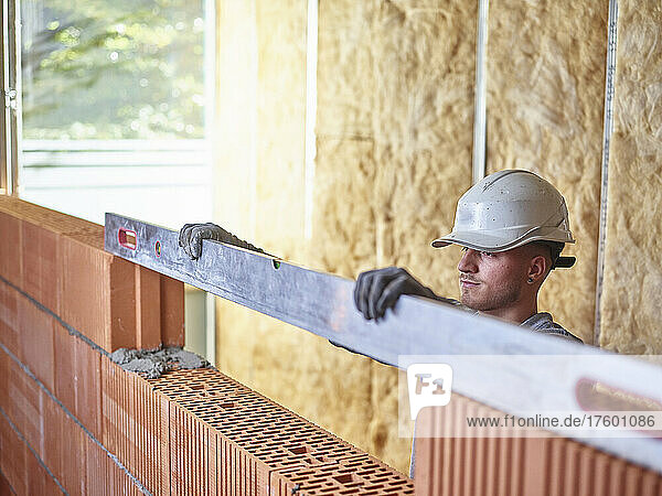Concentrated bricklayer using spirit level to measure bricks at construction site