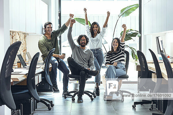 Cheerful multiracial businessmen and businesswomen with arms raised in coworking office
