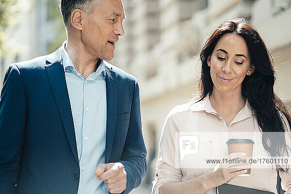 Businessman talking with businesswoman holding disposable coffee cup on sunny day