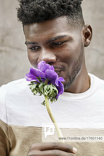 Portrait of a smiling young African American man smelling a purple flower on a brown background