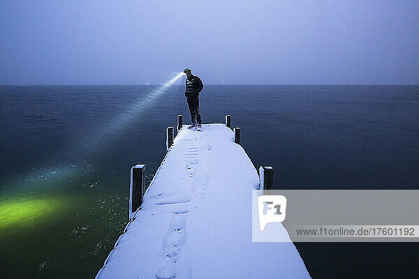 Hiker with headlamp standing on snow covered jetty at dusk  Walchensee  Bavaria  Germany