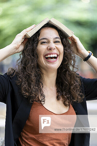 Young woman laughing and holding book on head