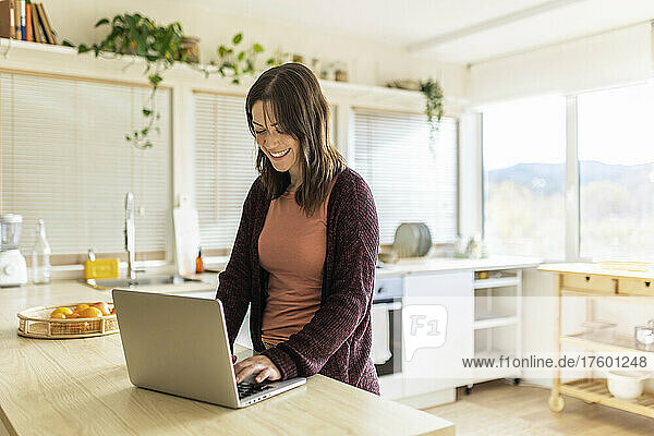 Smiling freelancer using laptop in kitchen at home
