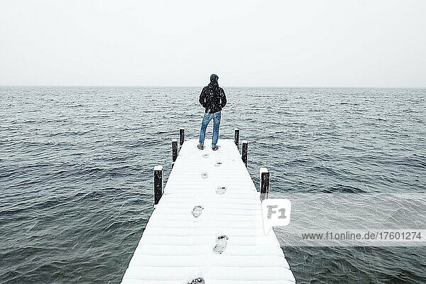 Hiker admiring lake standing on snow covered jetty in winter  Walchensee  Bavaria  Germany