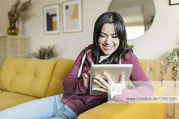 Happy woman using tablet PC sitting on sofa at home