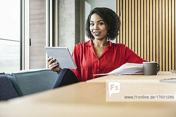 Young businesswoman with tablet computer and coffee on desk at work place