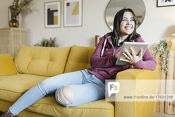 Happy young woman with tablet PC sitting on sofa in living room