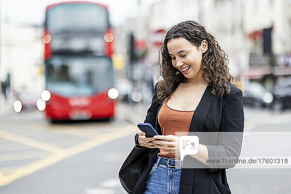 Glückliche Geschäftsfrau  die in der Stadt ihr Mobiltelefon benutzt