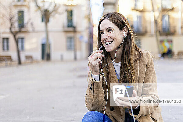 Happy woman with brown hair talking on smart phone through in-ear headphones