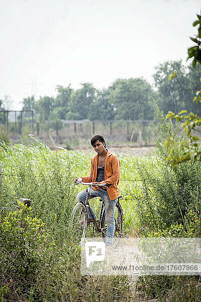 Porträt eines jungen Mannes  der auf seinem Fahrrad am Rande einer Wiese sitzt und in die Kamera schaut; Nagli Village Noida  Noida  Uttar Pradesh  Indien