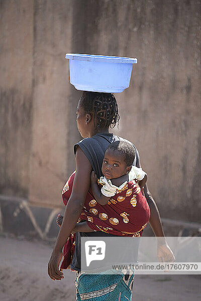 A Congolese woman with infant carries a plastic container on her head.; Kinshasa  Democratic Republic of the Congo.