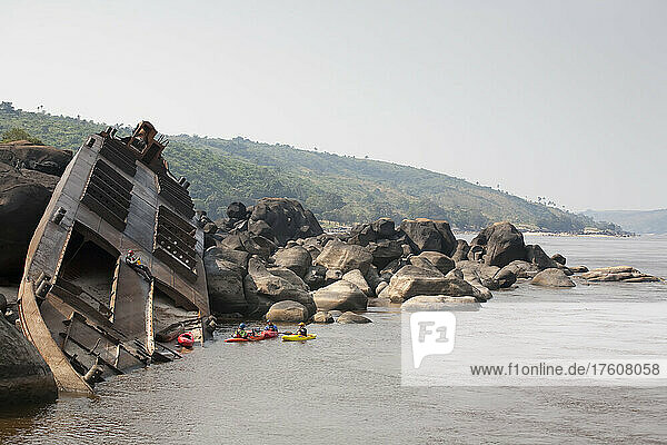 The kayakers eddy out to inspect the wreck of a barge.; Congo River  Democratic Republic of the Congo.