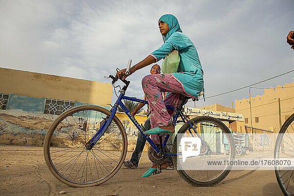 In Rissani  Marokko  geht ein kleiner Junge lächelnd spazieren  während ein Mädchen neben ihm Fahrrad fährt; Rissani  Marokko