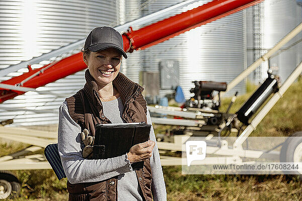 Ausschnitt aus dem Porträt einer Landwirtin  die fröhlich lächelt  während sie ein digitales Tablet in der Hand hält und auf einem modernen Bauernhof steht; Alcomdale  Alberta  Kanada