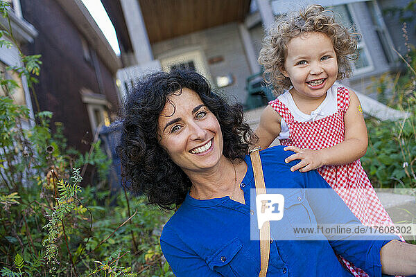 Mother and young daughter with big smiles for the camera outside their home; Toronto  Ontario  Canada