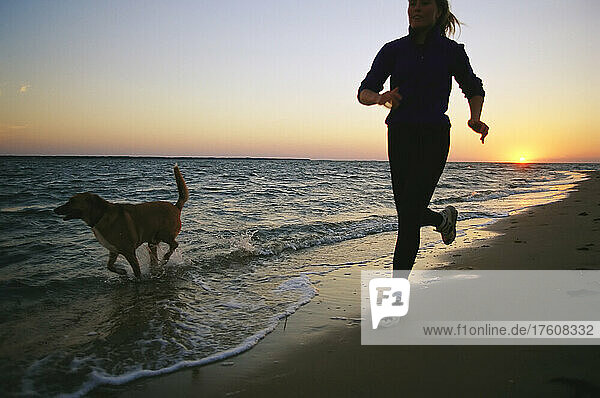 A woman and her dog run on the beach at sunset.; Nags Head  North Carolina.