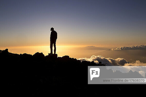Ein Mann steht bei Sonnenuntergang über dem Haleakala-Krater.
