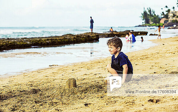 A young boy sitting in the sand at the water's edge on a beach in Ka'alapali and looking out to the ocean; Ka'anapali  Maui  Hawaii  United States of America