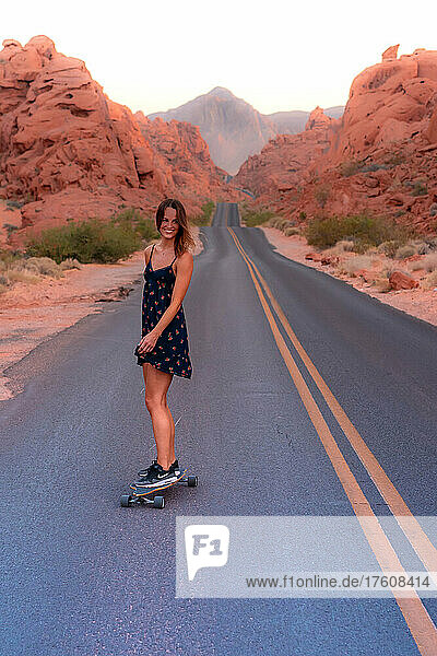 Eine Frau fährt mit dem Skateboard eine leere Wüstenstraße im Valley of Fire State Park hinunter.