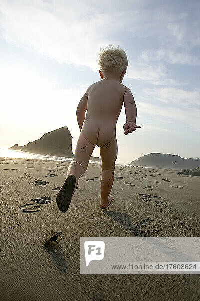 Ein zweijähriger Junge rennt nackt an einem Sandstrand entlang; Pistol River  Oregon.
